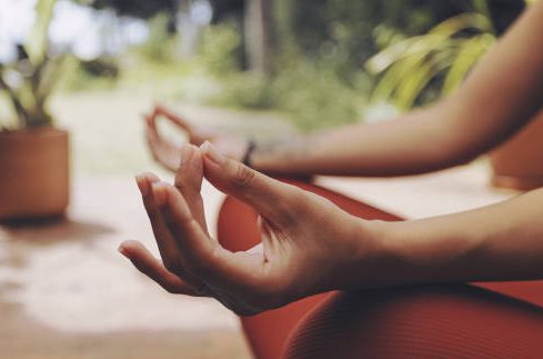 Meditatie Een hand in meditatiehouding met groenere omgeving op de achtergrond.